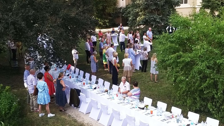 Menschen bei einer Gartenfeier mit langen, gedeckten Tischen im Freien.
