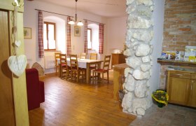 Gemütlicher Essbereich mit Holztisch und Stühlen, roten Vorhängen und Steinmauer.