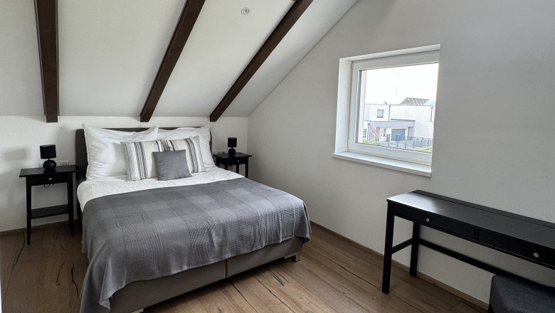 Modernes Schlafzimmer mit Holzbalkendecke, Doppelbett, Holzboden und Fenster.