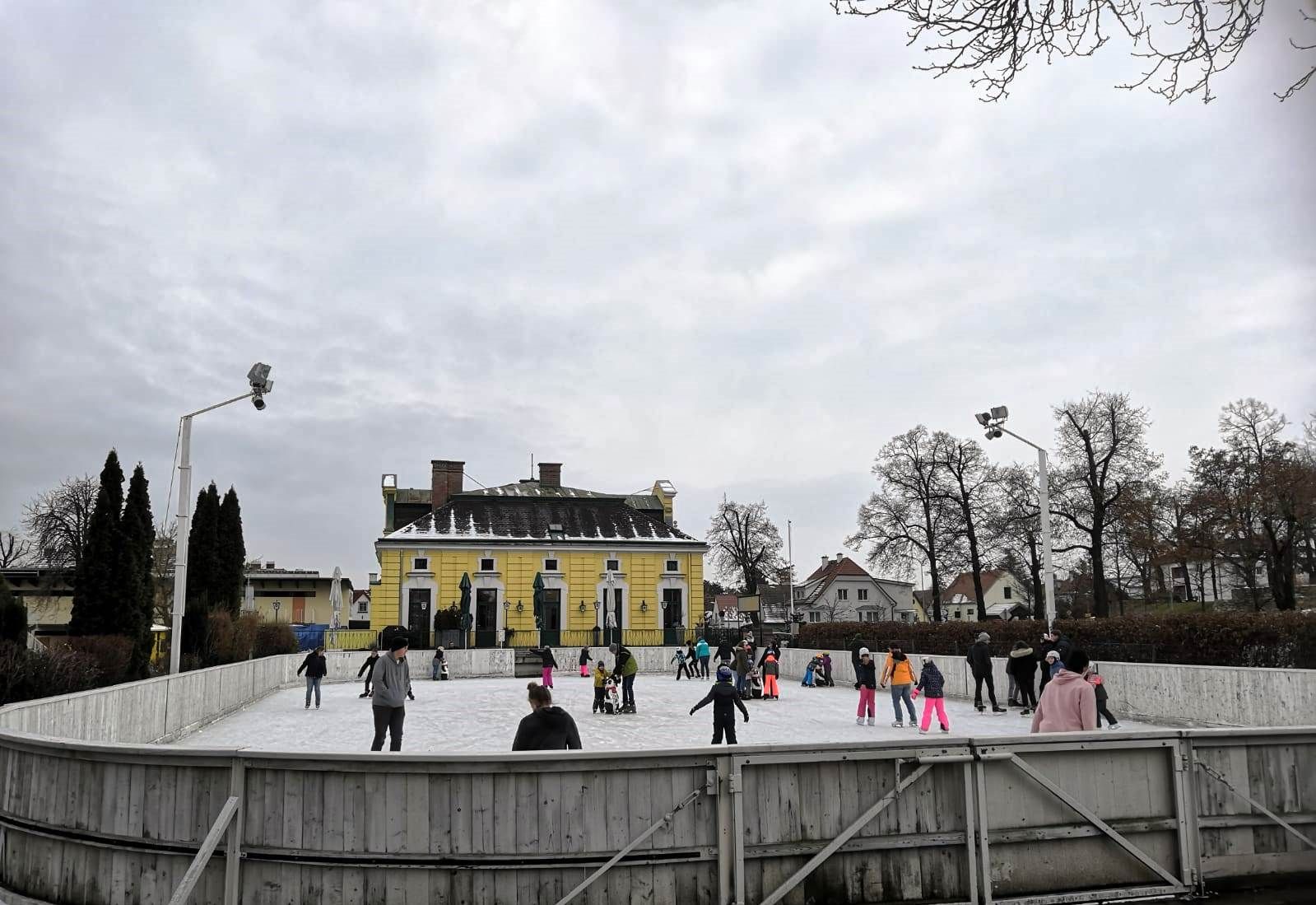 Menschen beim Eislaufen auf einem Freiluftplatz vor einem gelben Gebäude.