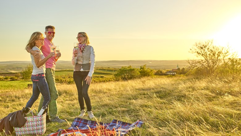 Drei Personen beim Picknick auf einer Wiese bei Sonnenuntergang.