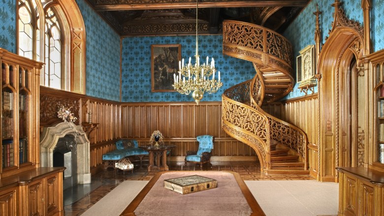 Innenansicht eines prunkvollen Raumes im Schloss Lednice mit Holztreppe, blauen Wänden und einem Kronleuchter.