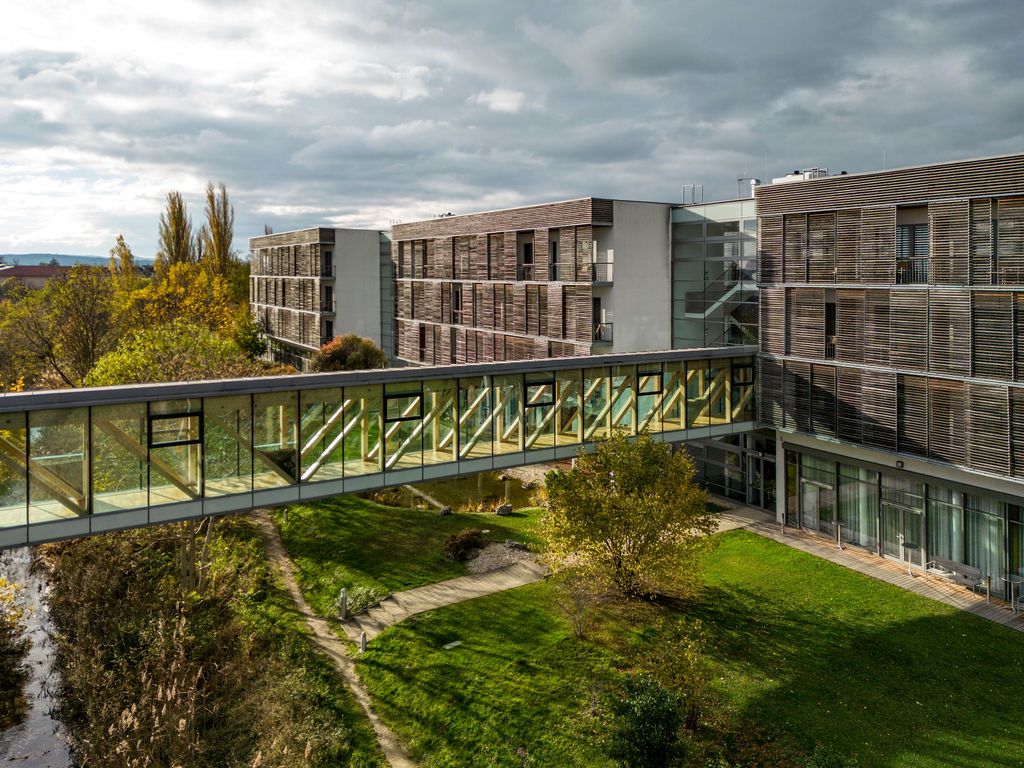 Glasüberdachter Übergang zwischen Therme Laa und Hotelgebäude, umgeben von grüner Landschaft.