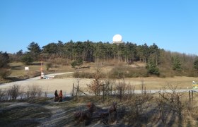 Landschaft mit H&uuml;gel, Wald und Radarkuppel unter blauem Himmel.