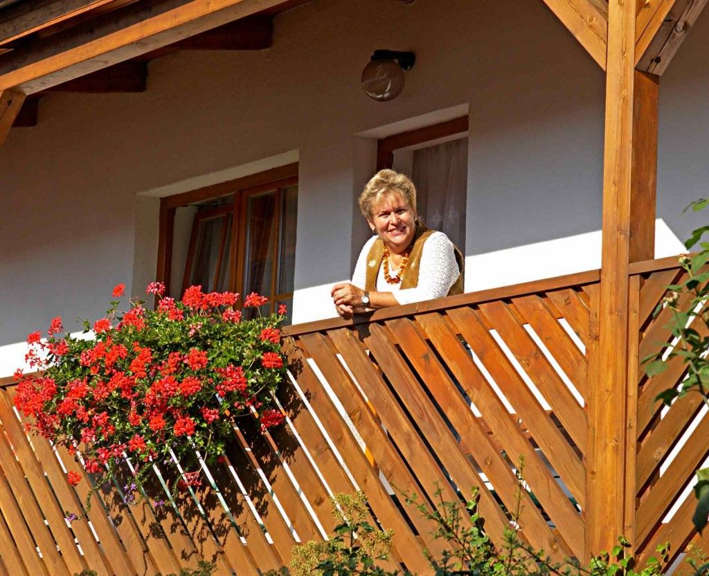 Eine Frau lehnt an einem Holzbalkon mit roten Blumen.