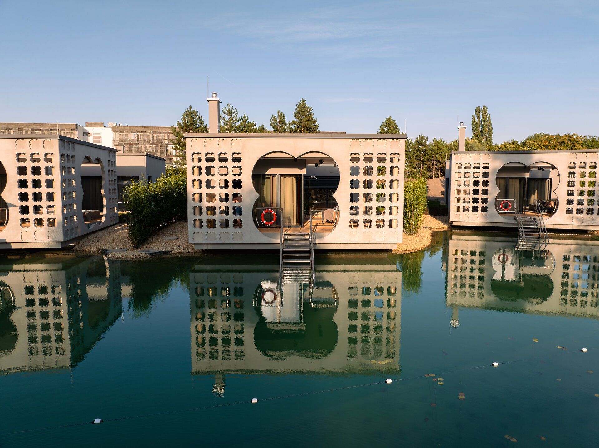 Die stilvollen Villen spiegeln sich im ruhigen Wasser und schaffen eine harmonische Atmosphäre der Entspannung. Umgeben von üppigem Grün und der sanften Brise, lädt dieser Ort dazu ein, die Seele baumeln zu lassen und die Schönheit der Natur zu genießen.