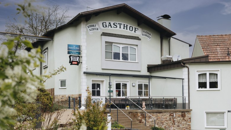 Außenansicht eines Gasthofs mit Terrasse und Treppe, umgeben von Pflanzen.