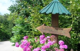 Holzschild mit Aufschrift 'Europakreuzweg' und rosa Blumen.