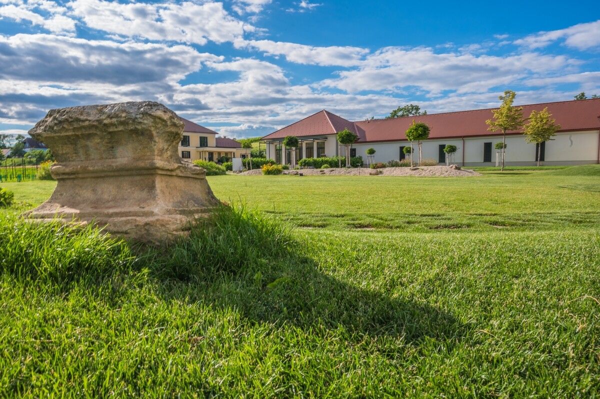 Weingut mit Rasenfläche und antikem Stein im Vordergrund.