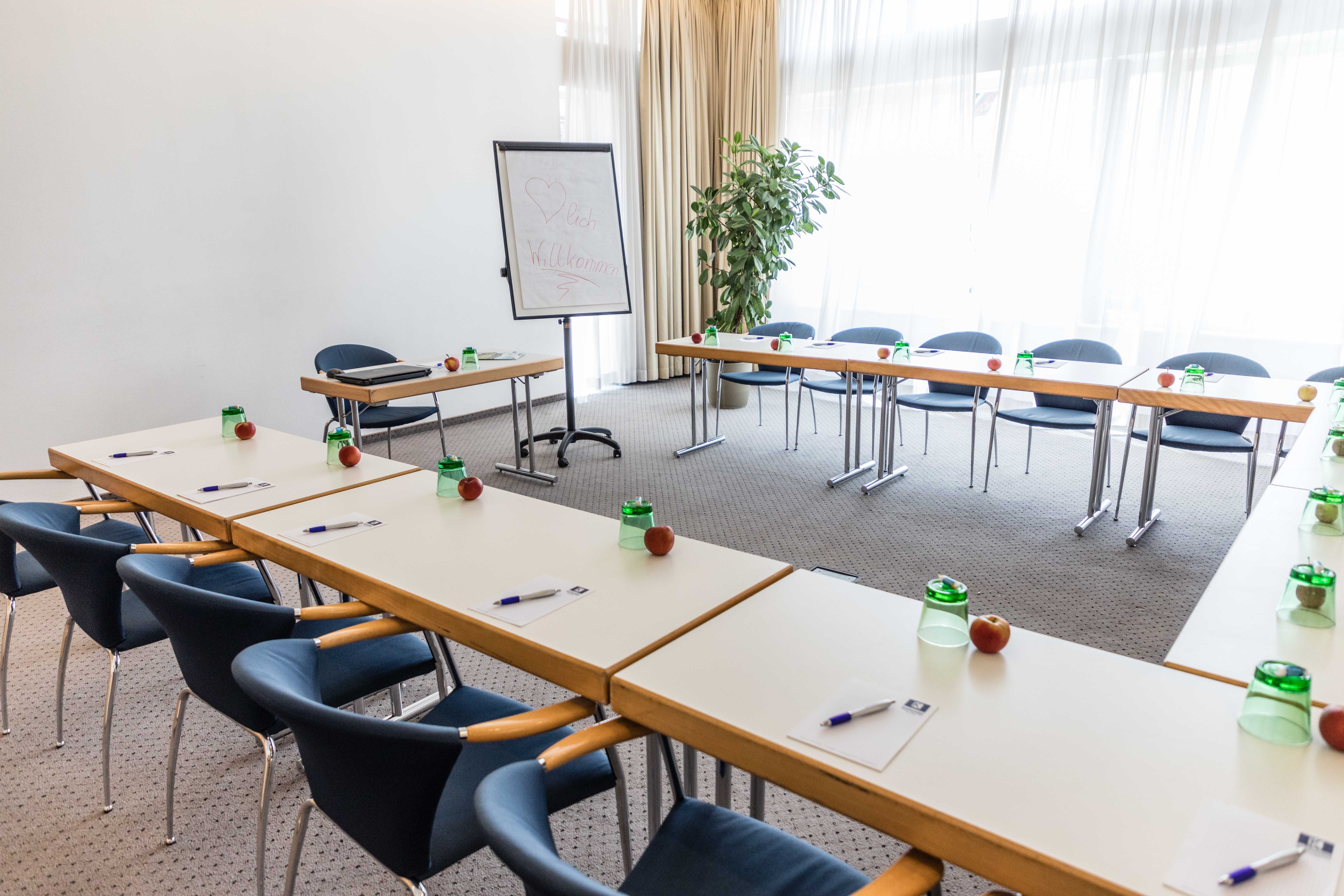 Konferenzraum mit Tischen in U-Form, Stühlen, Flipchart und Schreibmaterialien.