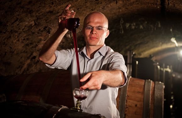 Vinař přelévá víno z jedné sklenice do druhé ve vinném sklepě.