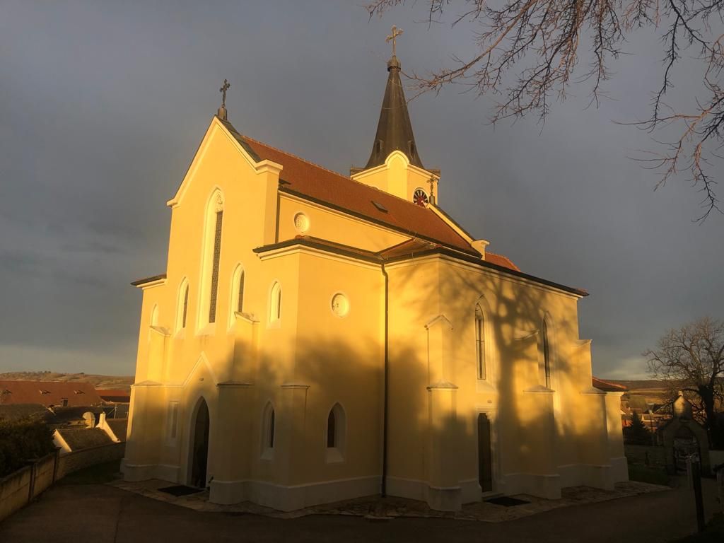 Gelbe Kirche in Glaubendorf im Sonnenlicht mit dunklem Himmel.