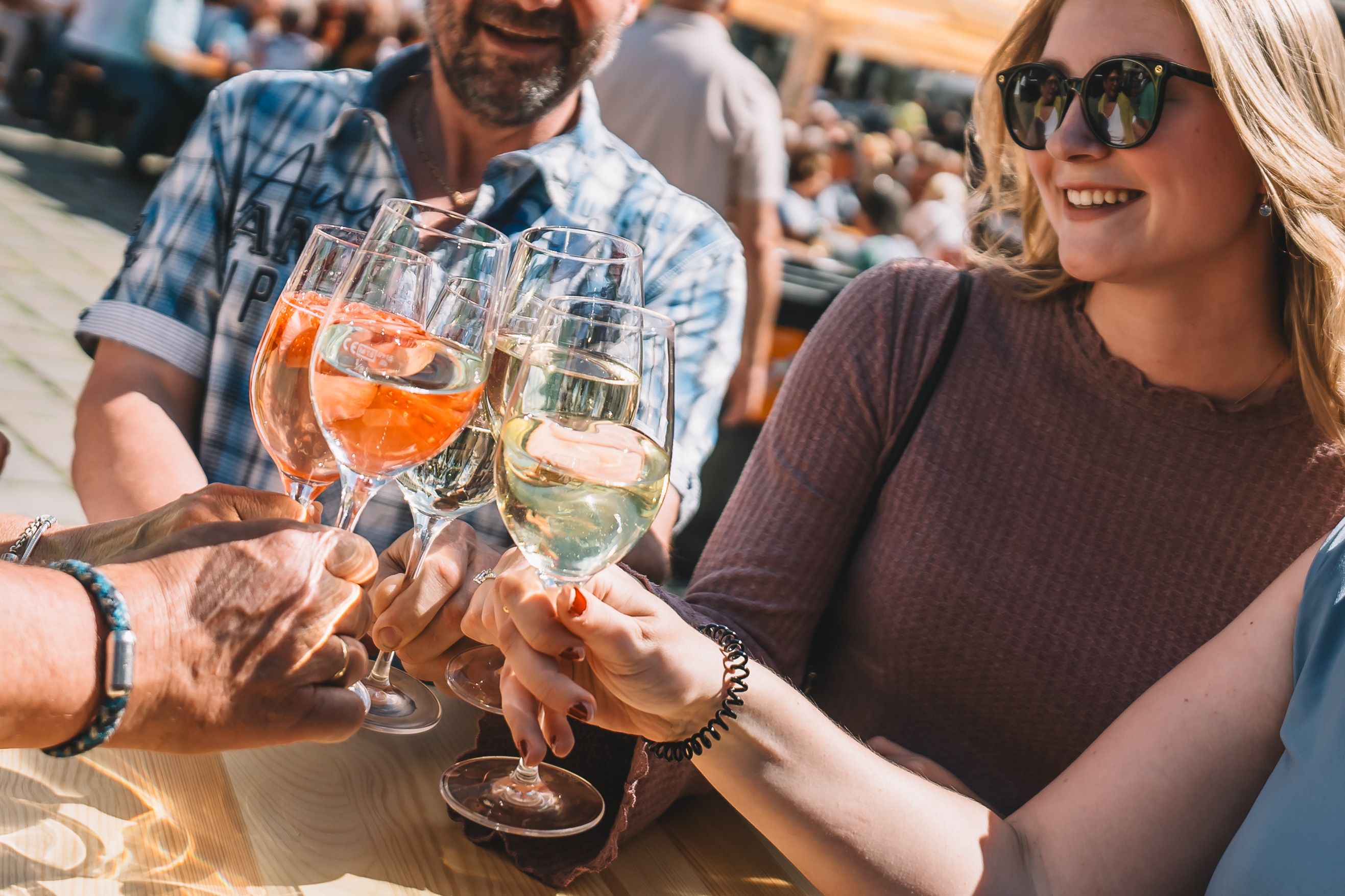 Lächelnde Personen stoßen bei Sonnenschein mit Weinviertler Wein in einer Innenstadt an. 
