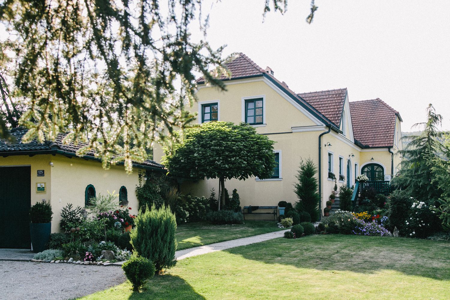 Gelbes Haus mit gepflegtem Garten und Bäumen im Vordergrund.