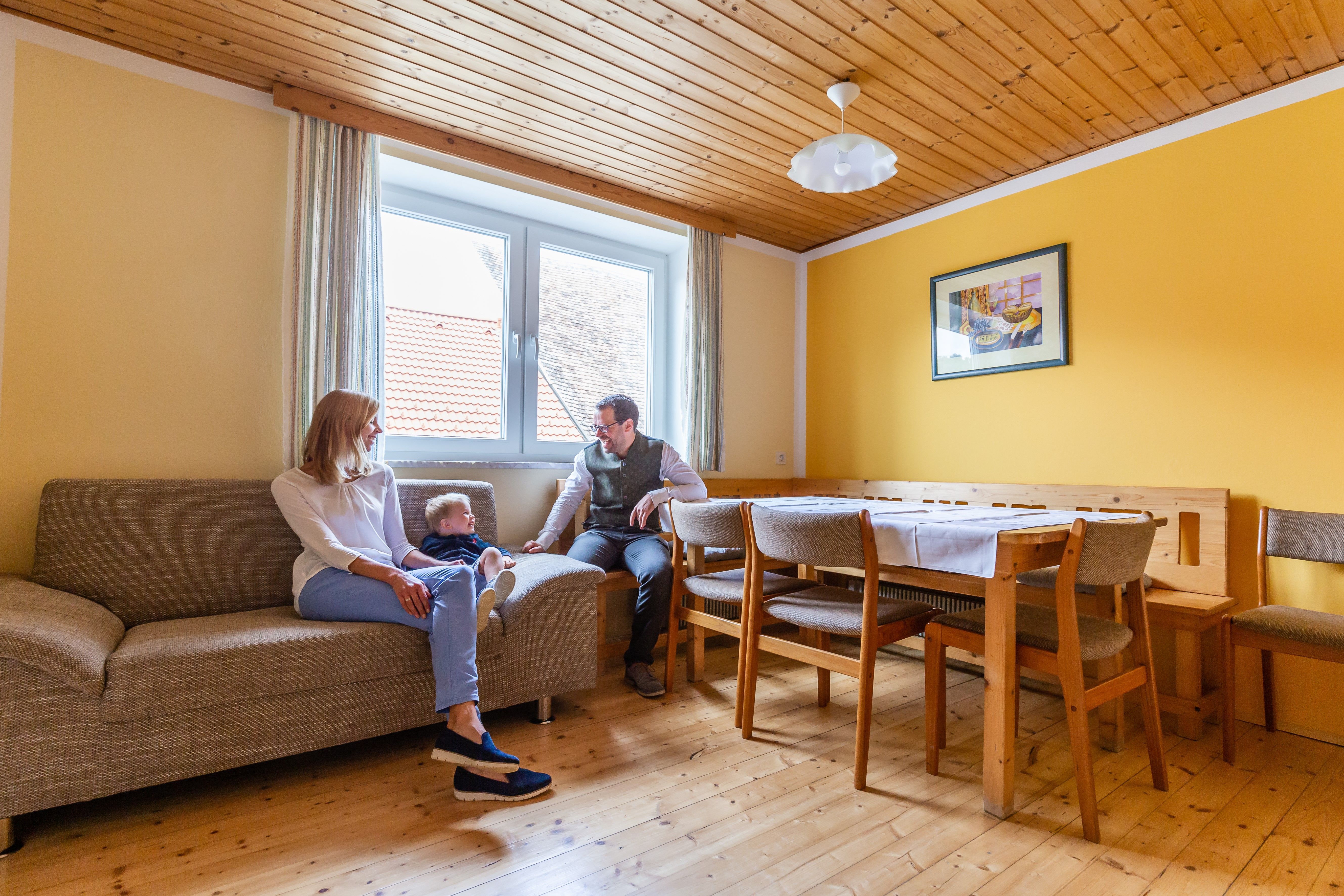 Familie sitzt in einem Wohnzimmer mit gelben Wänden und Holzmöbeln.