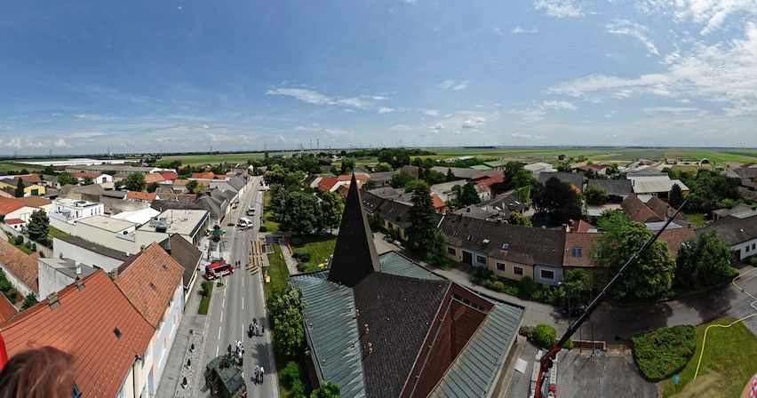 Blick über Aderklaa mit Dorfhäusern, Straße, Kirchturm und weitem Himmel über Feldern.