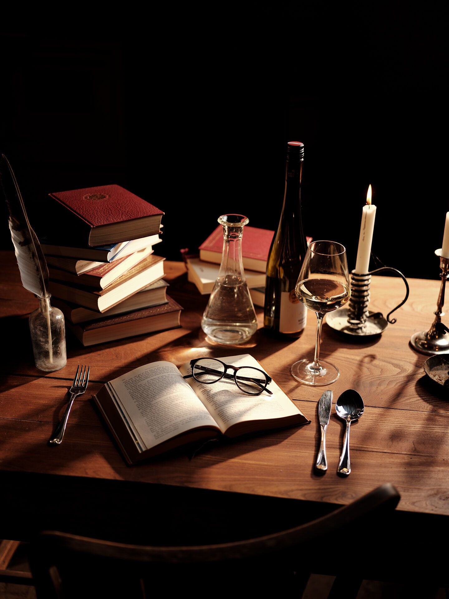 Ein einladendes Stillleben, das die Essenz des Weinherbstes einfängt. Auf einem rustikalen Holztisch liegen Bücher, eine elegante Karaffe und ein Glas Wein, umgeben von Kerzenlicht, das eine warme Atmosphäre schafft. Diese Szenerie lädt dazu ein, die kulinarischen Köstlichkeiten der Region in vollen Zügen zu genießen.