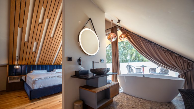 Modernes Hotelzimmer mit Holzdecke, freistehender Badewanne und Balkon.