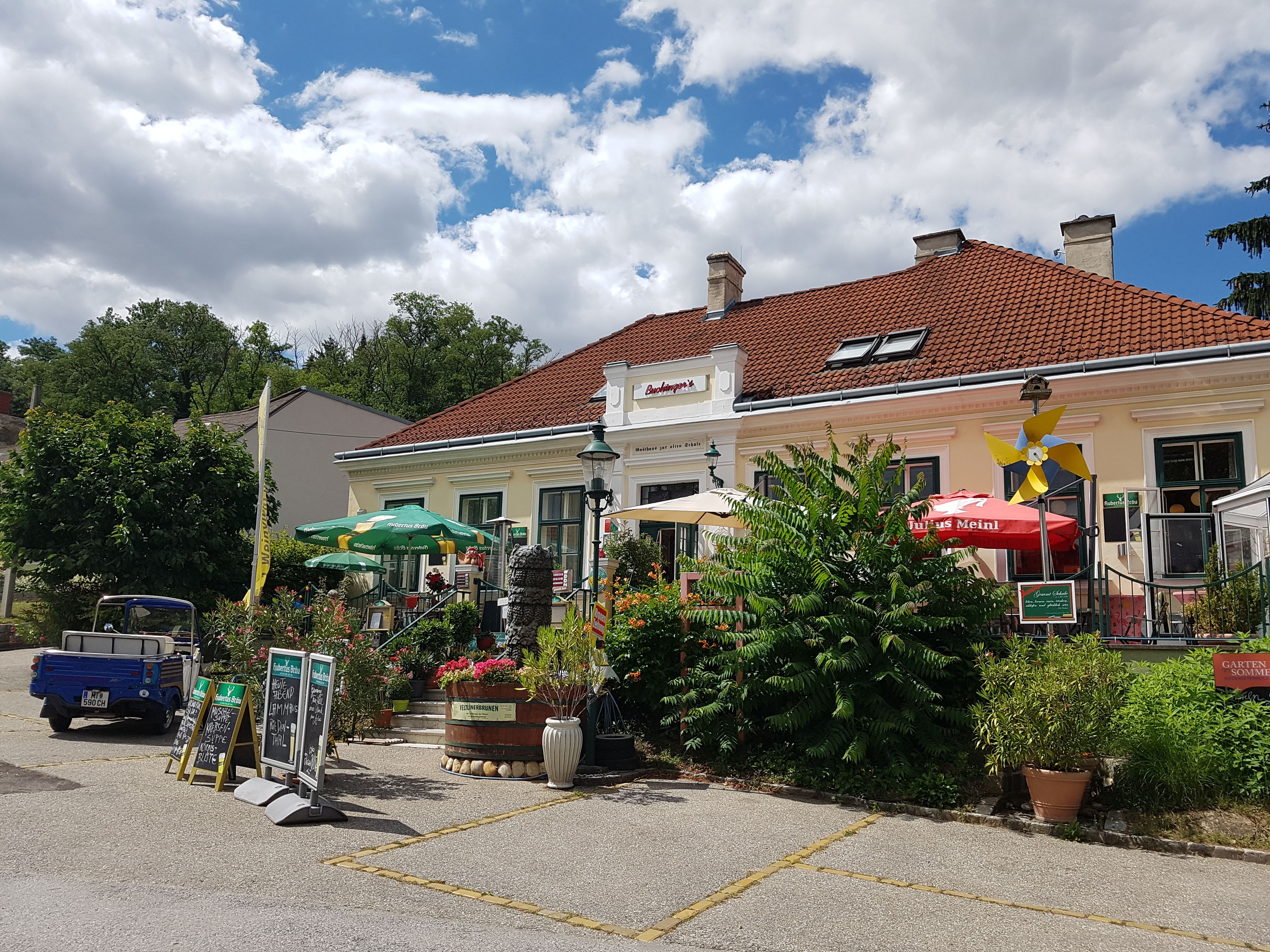 Außenansicht von Buchingers Gasthaus Zur Alten Schule mit Terrasse und Sonnenschirmen.