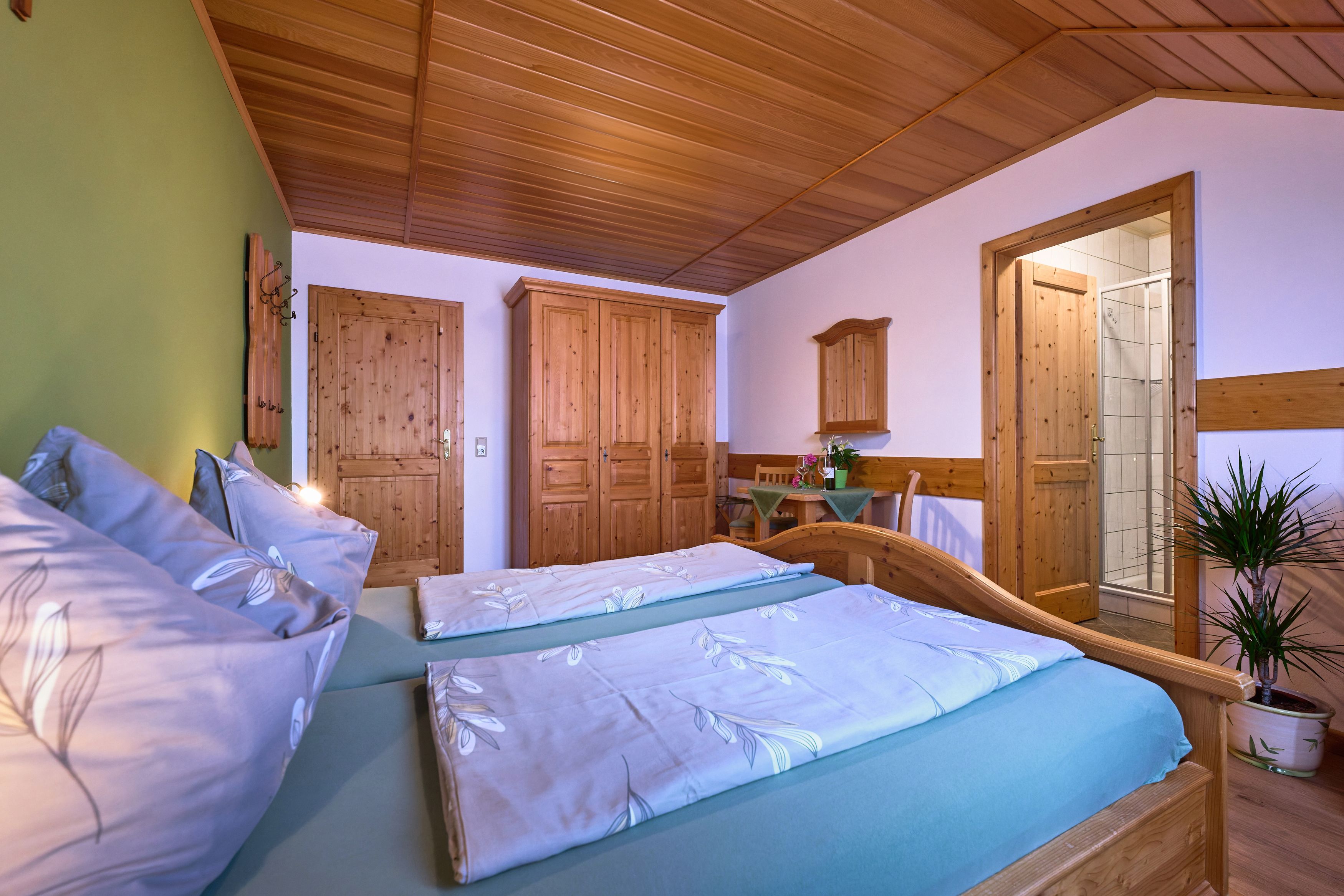 Gemütliches Schlafzimmer mit Holzmöbeln, Doppelbett, Kleiderschrank und kleinem Tisch. Eine Tür führt zu einem Badezimmer.