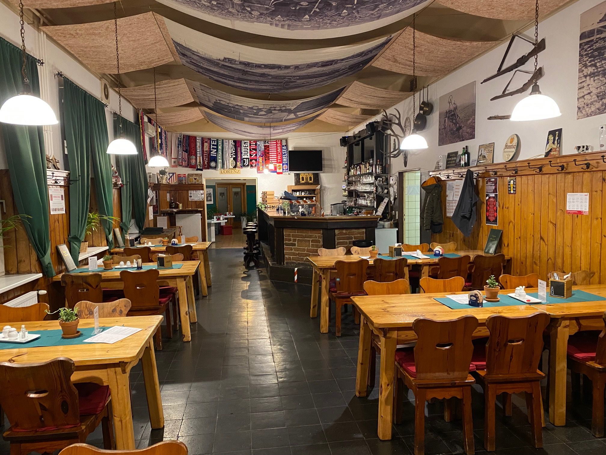 Gemütliche Gaststube mit Holztischen, Stühlen und Bar, dekoriert mit Fußballschals und rustikalen Elementen.