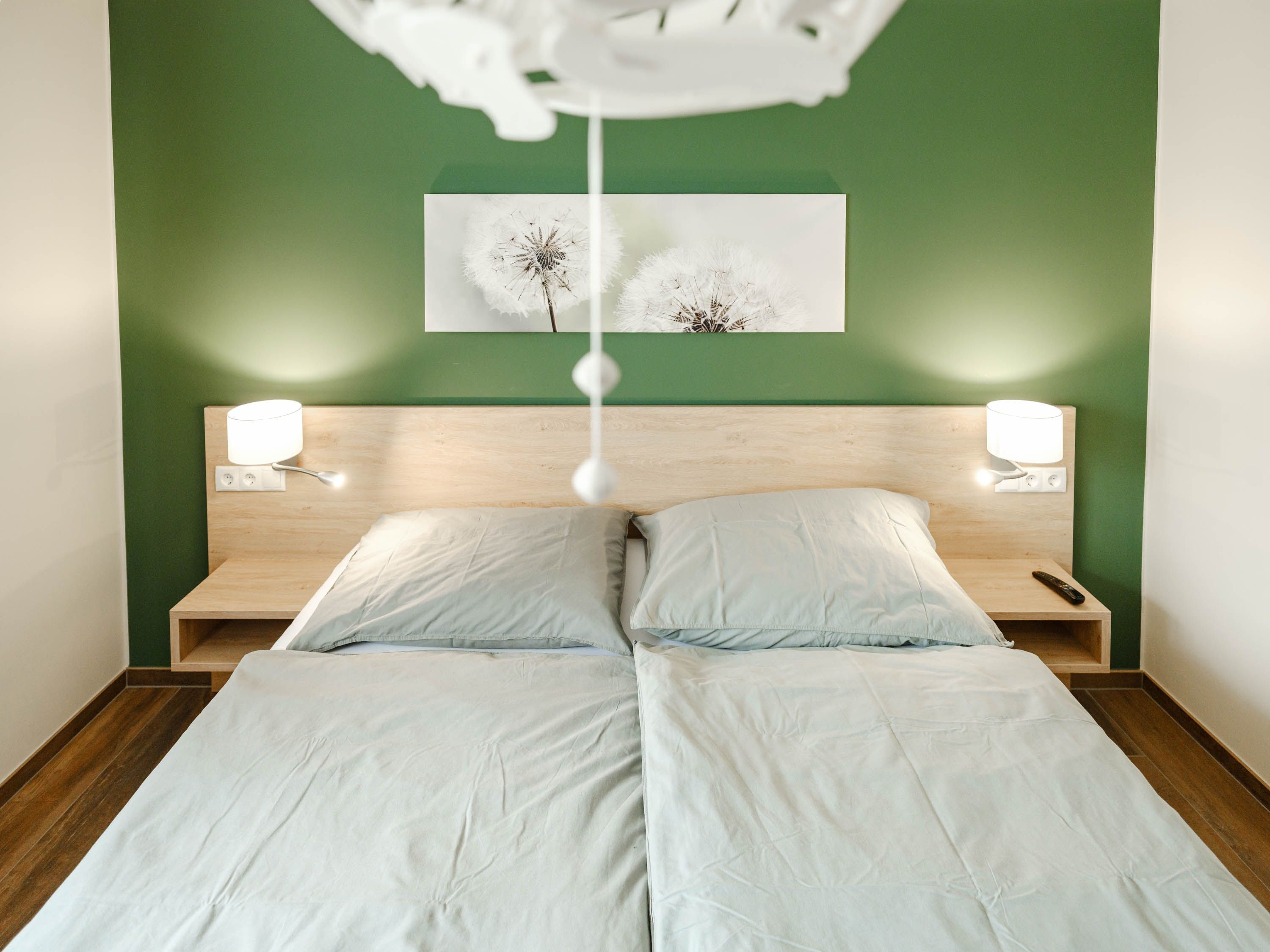 Modernes Schlafzimmer mit grün gestrichener Wand, Doppelbett und zwei Nachttischlampen.