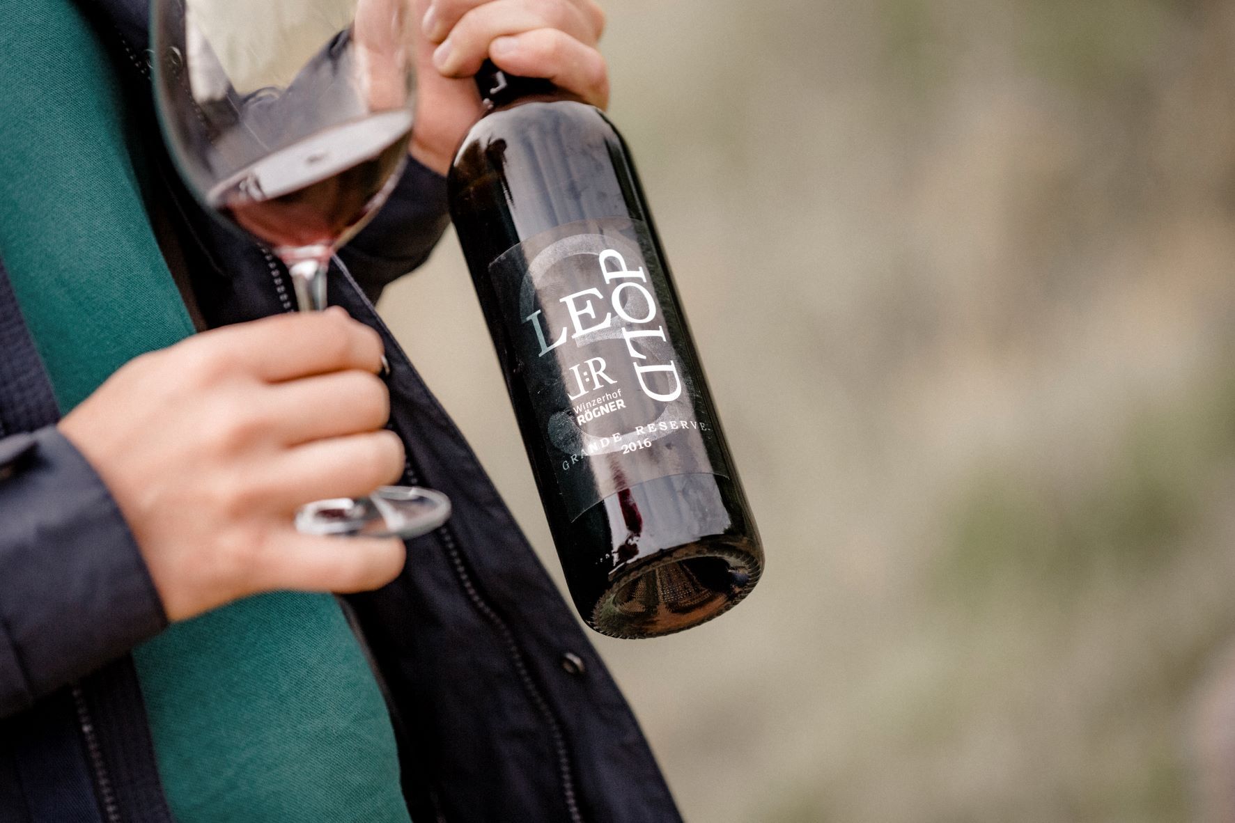 Person hält eine Weinflasche und ein Glas Rotwein.