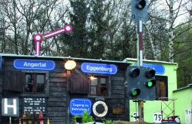 Modelleisenbahn mit Zügen vor einem kleinen Gebäude mit Schildern 'Angertal' und 'Eggenburg'.