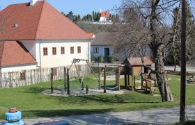 Ein Kinderspielplatz mit Klettergerüst und Schaukel neben einem Gebäude mit rotem Dach.
