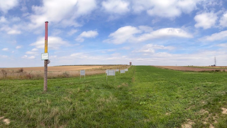 Wide landscape with a colorful post and several signs on a meadow under a blue sky.