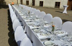 Lange, festlich gedeckte Tafel im Freien vor einem historischen Gebäude.