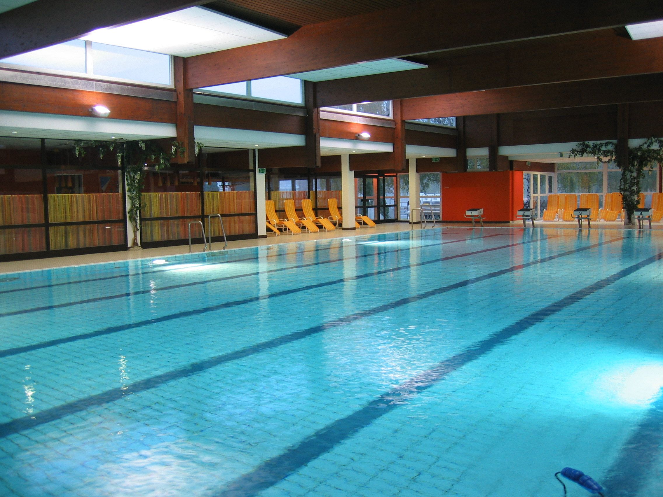 Innenansicht eines Schwimmbads mit leeren Liegestühlen am Beckenrand.