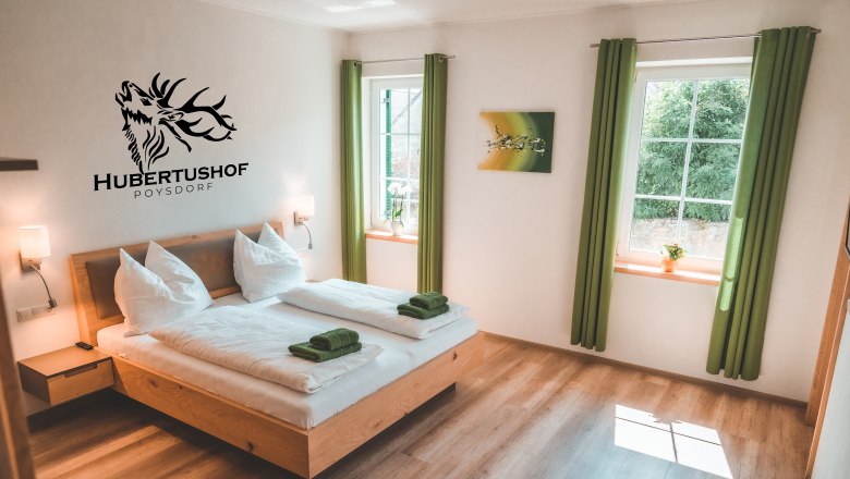 Modernes Gästezimmer mit Doppelbett, grünen Vorhängen und Wanddekoration im Hubertushof Poysdorf.