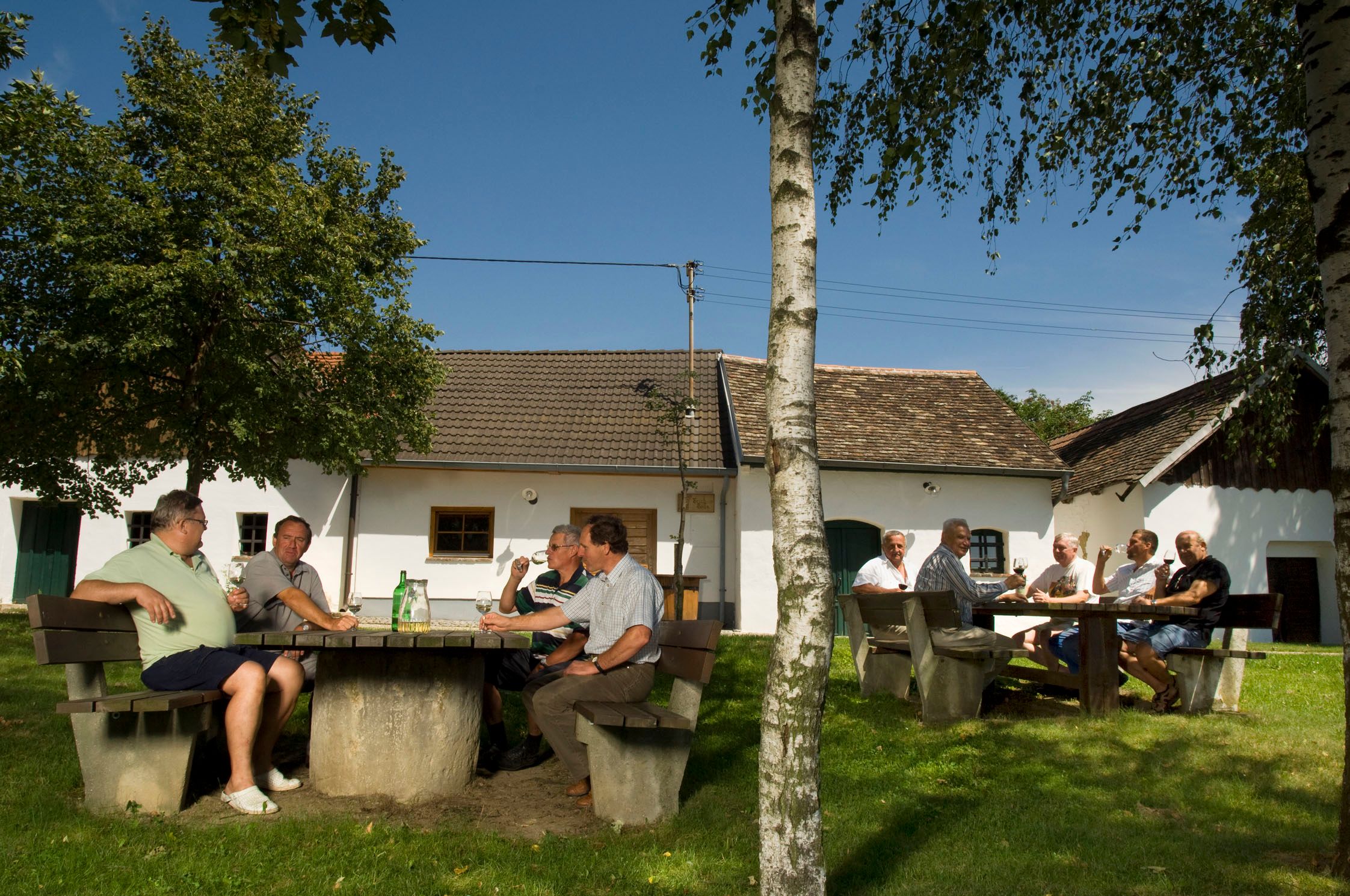 Menschen sitzen an Tischen im Freien vor traditionellen Gebäuden in Schöngrabern.