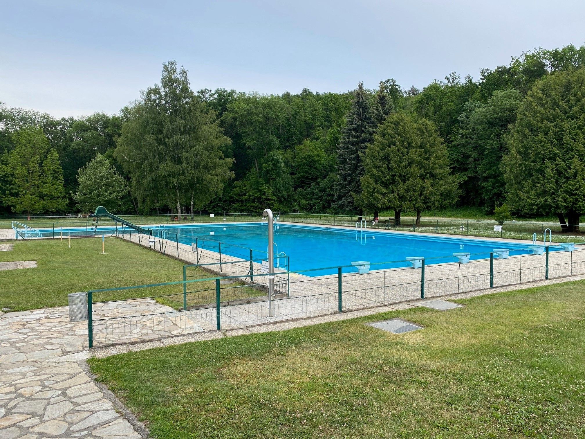 An empty outdoor pool with a large swimming pool, surrounded by trees and lawns.