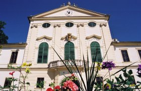 Fassade von Schloss Kirchstetten mit grünen Fensterläden und Blumen im Vordergrund.