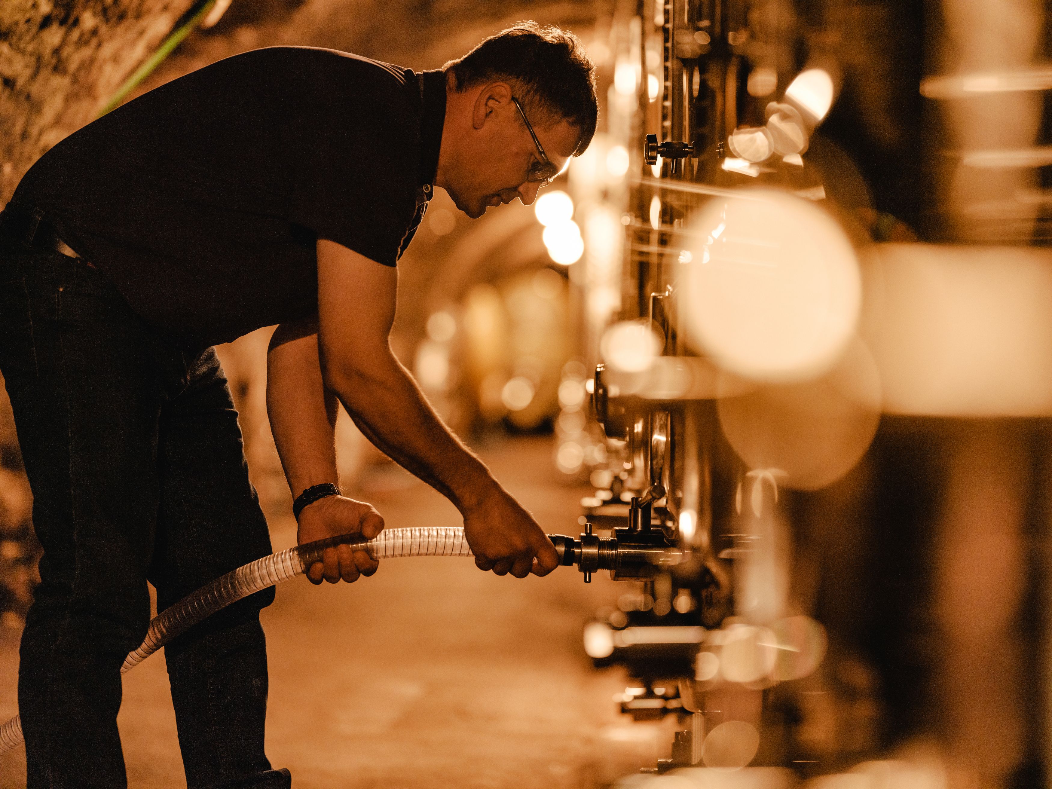 Person works in a wine cellar with tanks.