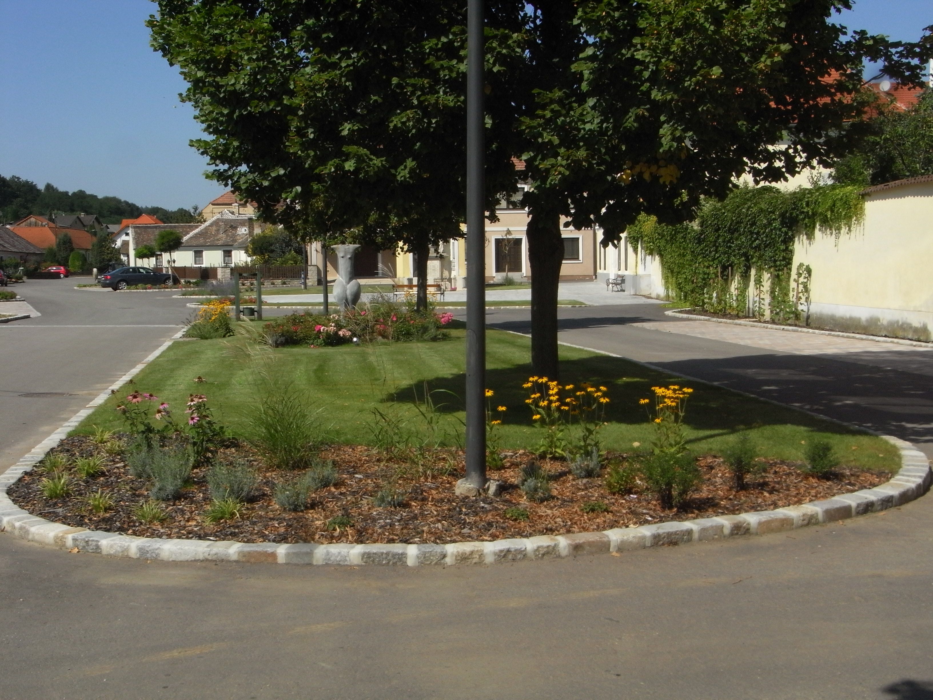 A well-kept flower bed with yellow flowers and trees in a quiet residential street.