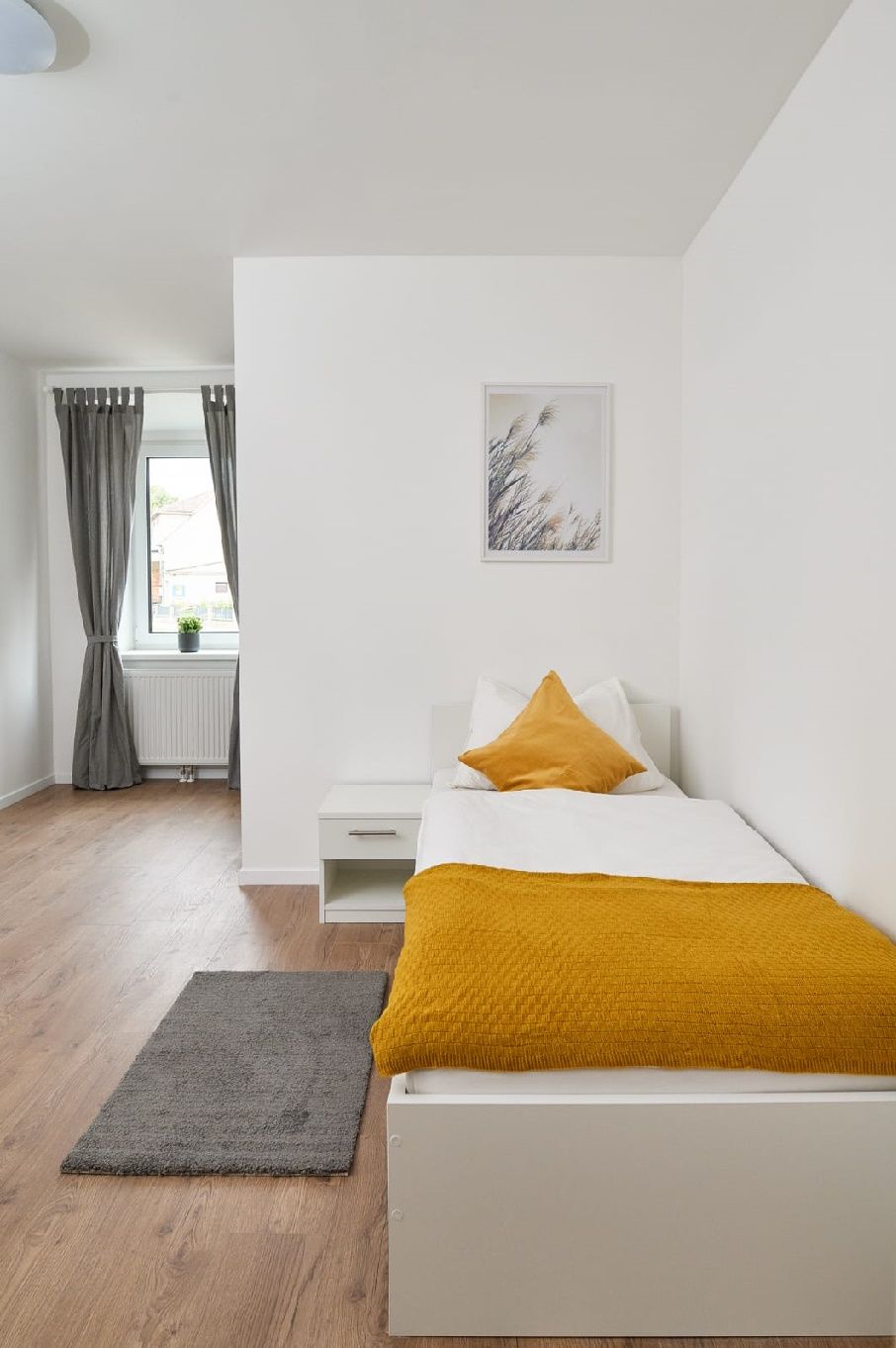 Einzelzimmer mit Bett, Nachttisch und Fenster mit Vorhängen.