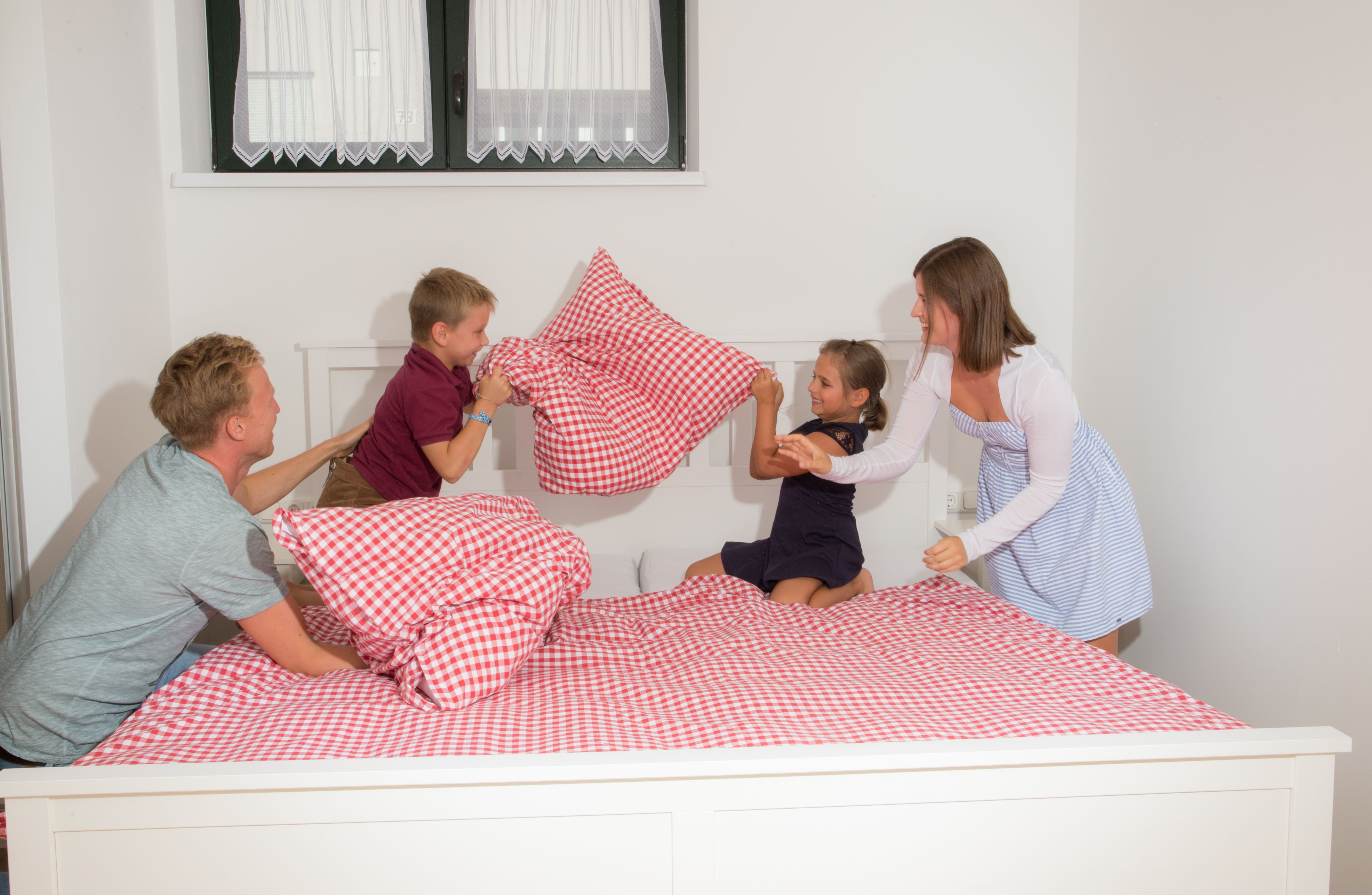 Familie hat Kissenschlacht auf einem Bett mit rot-weiß kariertem Bettzeug.