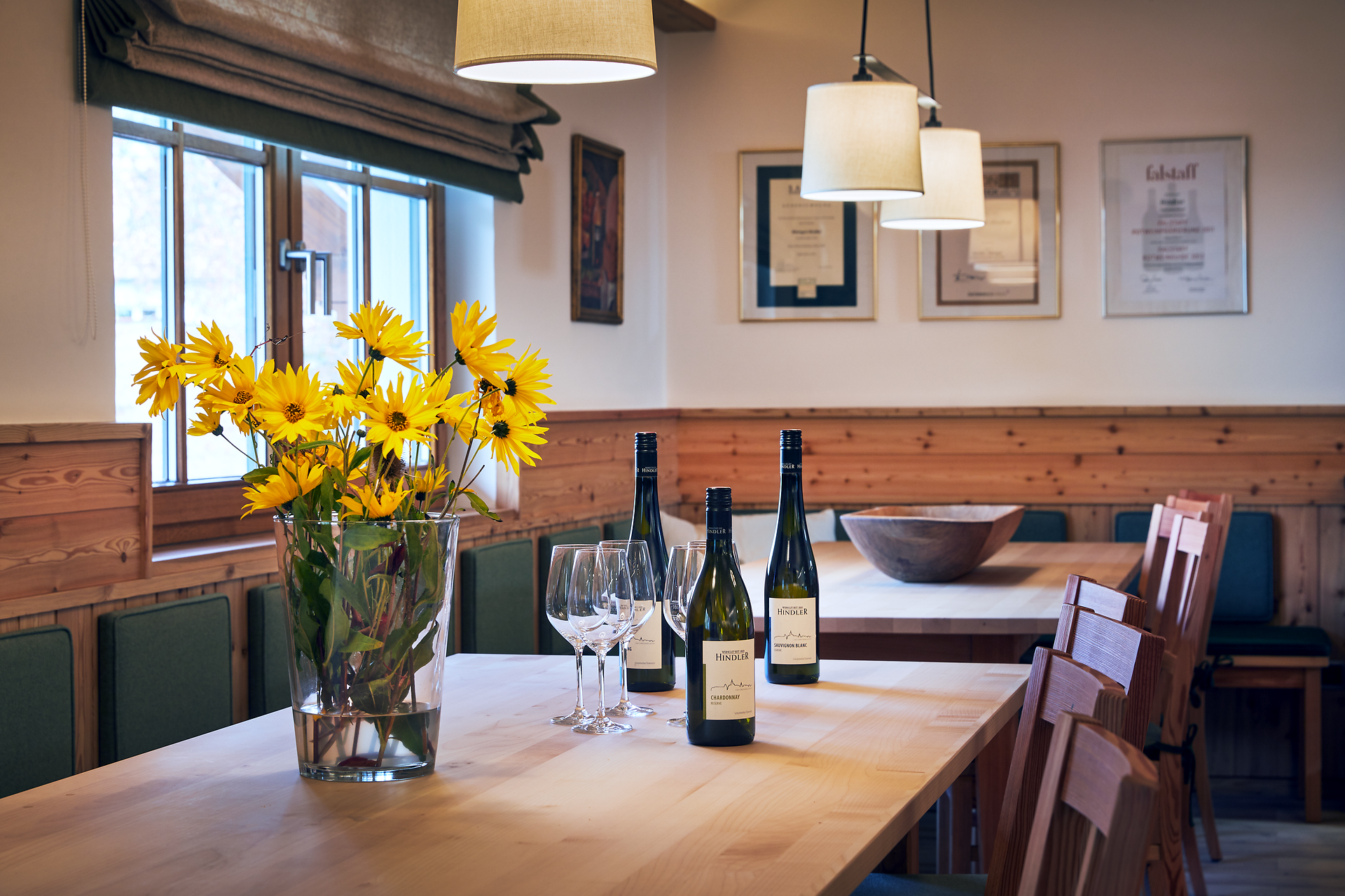 In einem einladenden Raum, umgeben von warmem Holz und sanftem Licht, entfaltet sich die Atmosphäre der Gemütlichkeit. Ein prächtiger Strauß Sonnenblumen bringt Farbe und Lebensfreude, während die eleganten Weinflaschen darauf warten, entdeckt zu werden. Hier wird der Genuss von Wein zu einem unvergesslichen Erlebnis.