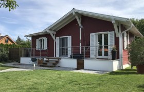 Ein rotes Holzhaus mit weißem Dach und Fensterläden, umgeben von einem gepflegten Garten.