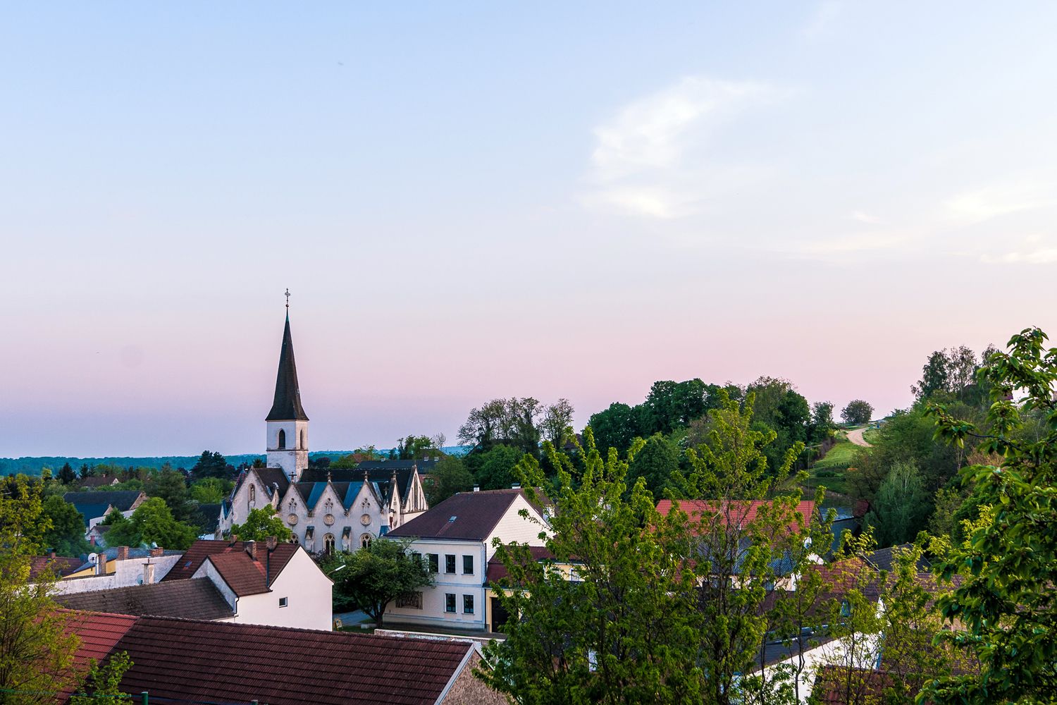 Blick auf die Kirche von Jedenspeigen bei Sonnenuntergang, umgeben von Bäumen und Häusern.