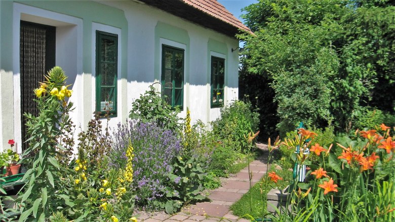 Ein gepflegter Garten mit bunten Blumen vor einem weißen Haus mit grünen Fensterrahmen.