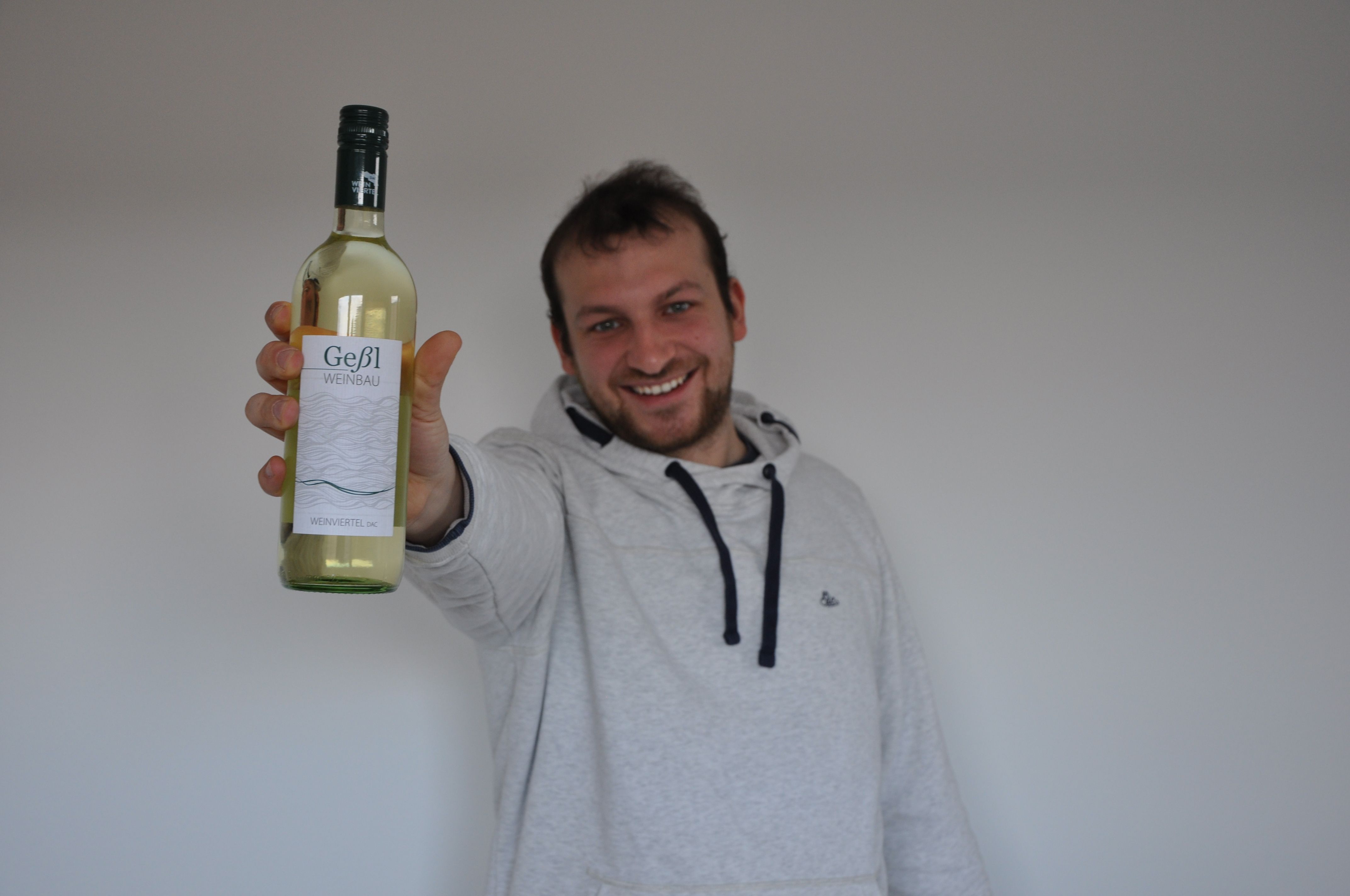 Muž drží před kamerou láhev bílého vína Geßl Weinbau.