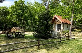 Eine kleine Kapelle mit rotem Dach in einem Waldgebiet, umgeben von Bäumen und einem Holzzaun.