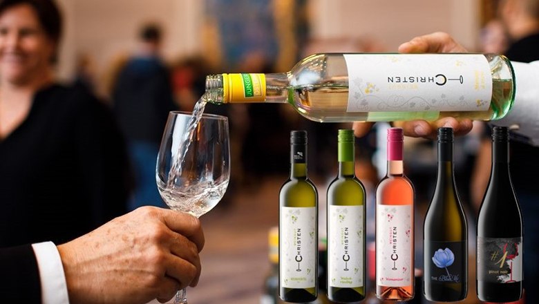 A hand pours white wine into a glass, with blurred people in the background. Below are six different bottles of wine from the Christen winery.