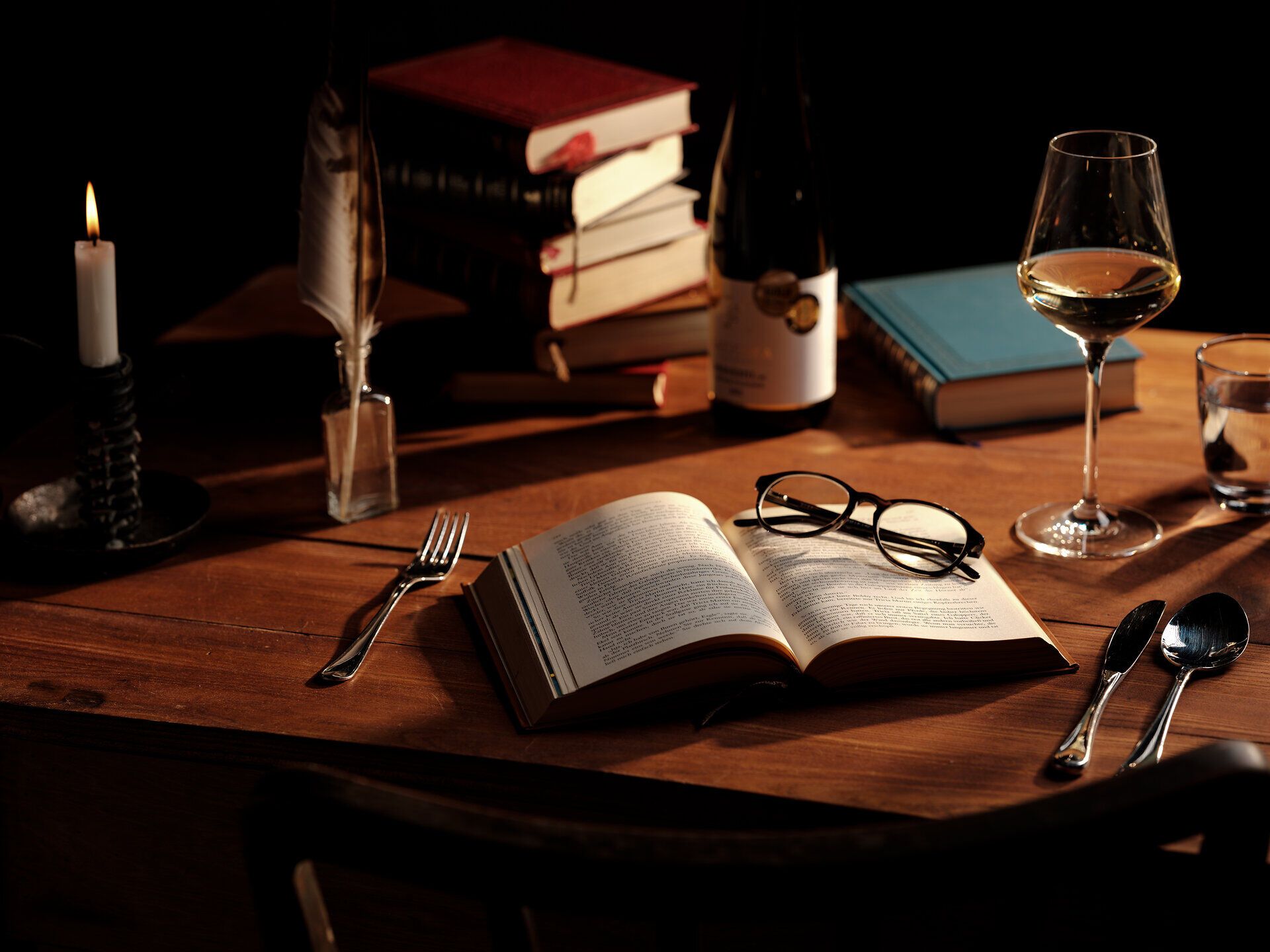 Ein einladender Tisch, geschmückt mit einem offenen Buch, einer eleganten Weinglas und einer Flasche Wein, lädt dazu ein, in die Welt der Kulinarik einzutauchen. Das sanfte Licht einer Kerze und die Präsenz von alten Büchern schaffen eine gemütliche Atmosphäre, die zum Verweilen und Genießen einlädt.