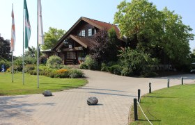 Eingang eines Golfclubs mit Holzgebäude und Fahnen.