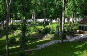 Ein gepflegter Garten mit Bäumen, Rasenflächen und einem kleinen Gebäude mit Terrasse.